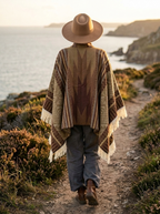 Poncho Éclat Nomade – coloris Camel, porté avec un chapeau sur un sentier côtier au coucher du soleil, vu de dos