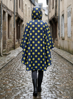 Poncho de Pluie Averse – coloris Marine à pois jaunes, porté capuche relevée dans une rue pavée sous la pluie, vu de dos